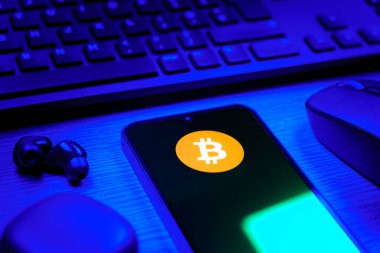 Prag, Çek Cumhuriyeti - 08 12 2025: Bitcoin logosunu gösteren klavyesi ve cep telefonu olan bir masanın yan görüntüsü. Bitcoin merkezi olmayan işlemler için dijital bir kripto para birimidir.