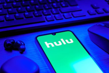 Prag, Çek Cumhuriyeti - 08 12 2025: Hulu logosunu gösteren klavyesi ve cep telefonu olan bir masanın yan görüntüsü. Hulu TV şovları, filmler ve canlı TV için bir yayın platformu..