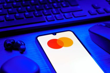 Prag, Çek Cumhuriyeti - 08 12 2025: Mastercard logosunu gösteren klavyesi ve cep telefonu olan bir masanın yan görüntüsü. Mastercard ödeme kartları ve hizmetler sağlayan bir finans şirketidir..