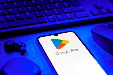Prag, Çek Cumhuriyeti - 08 12 2025: Google Play logosunu gösteren klavyesi ve cep telefonu olan bir masanın yan görüntüsü. Google Play uygulamaları, oyunları ve dijital içeriği indirmek için bir platformdur.
