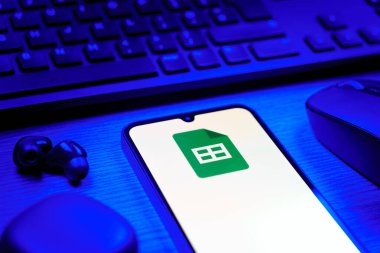 Prag, Çek Cumhuriyeti - 08 12 2025: Google Sheets logosunu gösteren klavyesi ve cep telefonu olan bir masanın yan görüntüsü. Google Sayfalar tablo oluşturmak ve yönetmek için bir platformdur.