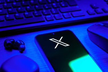 Prague, Czechia - 08 12 2025: A side view of a desk with a keyboard and a mobile phone displaying the X logo. X is a platform for sharing short posts and updates.