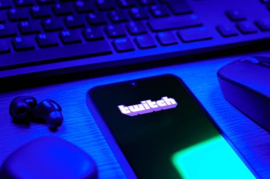 Prague, Czechia - 08 12 2025: A side view of a desk with a keyboard and a mobile phone displaying the Twitch logo. Twitch is a platform for live streaming games and content.