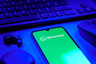 Prague, Czechia - 08 12 2025: A side view of a desk with a keyboard and a mobile phone displaying the WhatsApp logo. WhatsApp is an app for sending texts, calls, and media.