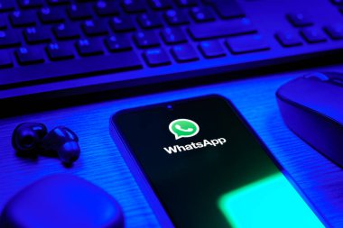 Prague, Czechia - 08 12 2025: A side view of a desk with a keyboard and a mobile phone displaying the WhatsApp logo. WhatsApp is an app for sending texts, calls, and media.