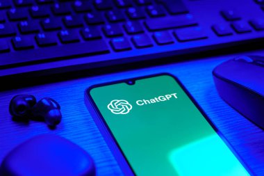 Prague, Czechia - 08 12 2025: A side view of a desk with a keyboard and a mobile phone displaying the ChatGPT logo. ChatGPT is an AI chatbot for generating text and answering questions.