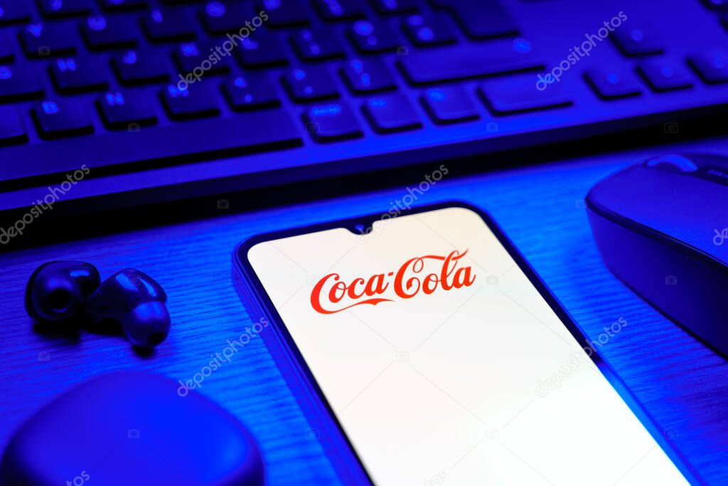 Prague, Czechia - 08 12 2025: A side view of a desk with a keyboard and a mobile phone displaying the Coca-Cola logo. Coca-Cola is a beverage company known for its soft drinks.
