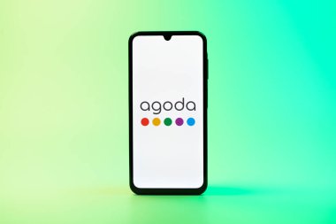 Prag, Çek Cumhuriyeti - 08 10 2025: Arka planda duran bir cep telefonu Agoda logosunu gösteriyor. Agoda, otelleri ve seyahat yerlerini ayırtmak için bir platform..