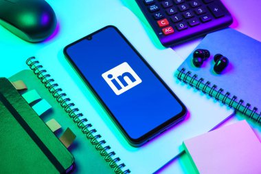 Prag, Çek Cumhuriyeti - 08 18 2025: Merkezde LinkedIn logosunu gösteren bir cep telefonu ile ofis malzemeleri düzenlemesi. LinkedIn, insanları ve şirketleri birbirine bağlayan profesyonel bir ağ..