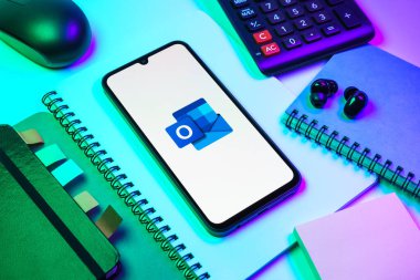 Prag, Çek Cumhuriyeti - 08 18 2025: Merkezde Outlook logosunu gösteren bir cep telefonu ile ofis malzemeleri düzenlemesi. Outlook iletileri göndermek ve yönetmek için bir e- posta platformudur.
