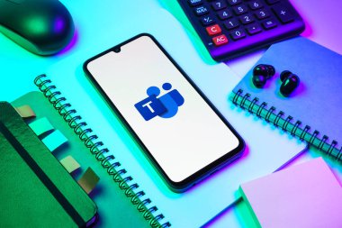 Prag, Çek Cumhuriyeti - 08 18 2025: Merkezde ekiplerin logosunu gösteren bir cep telefonu ile ofis malzemeleri düzenlemesi. Takımlar takım işbirliği, toplantılar ve iletişim için bir platformdur..