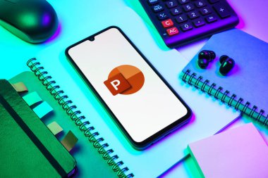 Prag, Çek Cumhuriyeti - 08 18 2025: Merkezde Powerpoint logosunu gösteren bir cep telefonu ile ofis malzemeleri düzenlemesi. Powerpoint sunumlar ve slayt gösterileri oluşturmak için bir yazılımdır..