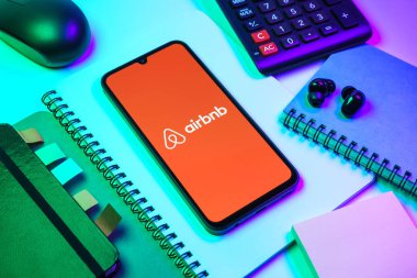 Prag, Çek Cumhuriyeti - 08 18 2025: Merkezde Airbnb logosu sergilenen bir cep telefonu ile ofis malzemeleri düzenlemesi. Airbnb dünya çapında kısa vadeli konaklama için bir platformdur..