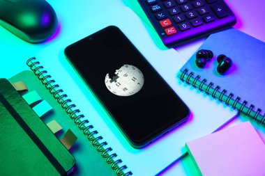 Prag, Çek Cumhuriyeti - 08 18 2025: Merkezinde Wikipedia logosu bulunan bir cep telefonu ile ofis malzemeleri düzenlemesi. Vikipedi çevrimiçi bir ansiklopedidir..