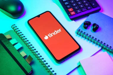 Prag, Çek Cumhuriyeti - 08 18 2025: Merkezde Tinder logosu sergilenen bir cep telefonu ile ofis malzemeleri düzenlemesi. Tinder insanları eşleştirmek ve bağlamak için bir randevu uygulaması.