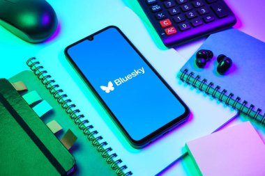 Prag, Çek Cumhuriyeti - 08 18 2025: Merkezde Bluesky logosunu gösteren bir cep telefonu ile ofis malzemeleri düzenlemesi. Bluesky merkezi olmayan ağlar için bir sosyal medya platformudur..