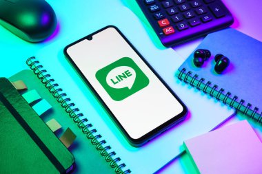 Prag, Çek Cumhuriyeti - 08 18 2025: Merkezinde hat logosu sergilenen bir cep telefonu ile ofis malzemeleri düzenlemesi. Line aramalar, mesajlar ve çokluortam paylaşımı için bir mesajlaşma uygulamasıdır.