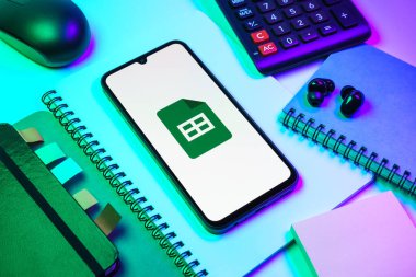 Prag, Çek Cumhuriyeti - 08 18 2025: Merkezde Google Sheets logosunu gösteren bir cep telefonu ile ofis malzemeleri düzenlemesi. Google Sayfalar tablo oluşturmak ve yönetmek için bir platformdur.