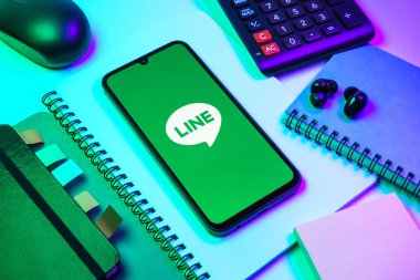 Prag, Çek Cumhuriyeti - 08 18 2025: Merkezinde hat logosu sergilenen bir cep telefonu ile ofis malzemeleri düzenlemesi. Line aramalar, mesajlar ve çokluortam paylaşımı için bir mesajlaşma uygulamasıdır.