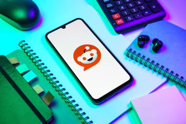 Prag, Çek Cumhuriyeti - 08 18 2025: Merkezde Reddit logosunu gösteren bir cep telefonu ile ofis malzemeleri düzenlemesi. Reddit tartışma, haber ve toplum içeriği için bir platformdur.