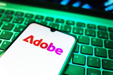 Prag, Çek Cumhuriyeti - 08 19 2025: Klavyede duran ve Adobe logosunu gösteren bir cep telefonunun yakından görüntüsü. Adobe yaratıcı araçlar ve hizmetler sunan bir yazılım şirketidir..