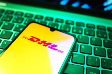 Prag, Çek Cumhuriyeti - 08 19 2025: DHL logosunu gösteren klavyenin üzerinde duran cep telefonunun yakından görüntüsü. DHL uluslararası nakliye hizmeti sunan bir lojistik şirketidir..