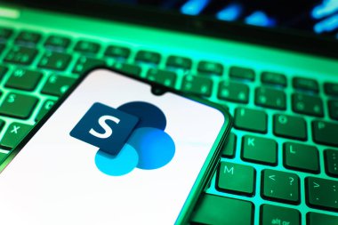 Prag, Çek Cumhuriyeti - 08 19 2025: Microsoft Sharepoint logosunu gösteren klavyenin üzerinde duran cep telefonunun yakından görüntüsü. Microsoft Sharepoint işbirliği ve belge yönetimi için bir platformdur.