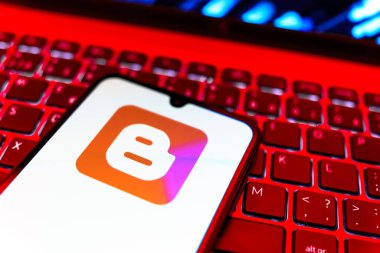 Prag, Çek Cumhuriyeti - 08 19 2025: Klavyenin üzerinde duran ve Blogger logosunu gösteren cep telefonunun yakından görüntüsü. Blogger blog oluşturma ve yayınlama için bir platformdur.