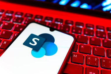 Prag, Çek Cumhuriyeti - 08 19 2025: Microsoft Sharepoint logosunu gösteren klavyenin üzerinde duran cep telefonunun yakından görüntüsü. Microsoft Sharepoint işbirliği ve belge yönetimi için bir platformdur.