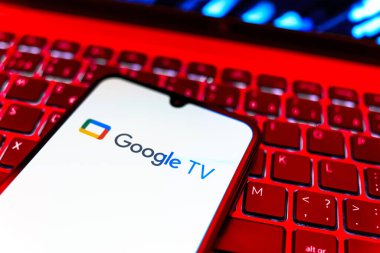 Prag, Çek Cumhuriyeti - 08 19 2025: Google TV logosunu gösteren klavyenin üzerinde duran bir cep telefonunun yakından görüntüsü. Google TV film, program ve uygulamalar için bir platformdur..