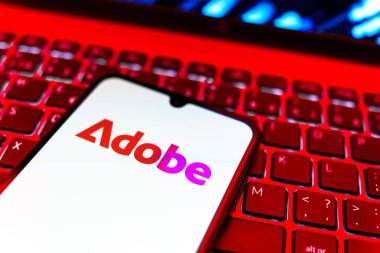 Prag, Çek Cumhuriyeti - 08 19 2025: Klavyede duran ve Adobe logosunu gösteren bir cep telefonunun yakından görüntüsü. Adobe yaratıcı araçlar ve hizmetler sunan bir yazılım şirketidir..