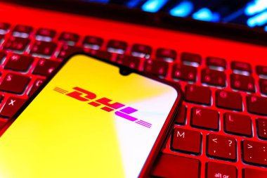 Prag, Çek Cumhuriyeti - 08 19 2025: DHL logosunu gösteren klavyenin üzerinde duran cep telefonunun yakından görüntüsü. DHL uluslararası nakliye hizmeti sunan bir lojistik şirketidir..