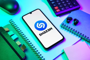 Prag, Çek Cumhuriyeti - 08 18 2025: Merkezinde Shazam logosu bulunan bir cep telefonu ile ofis malzemeleri düzenlemesi. Shazam şarkıları ve müzik parçalarını tanımlamak için bir uygulamadır.