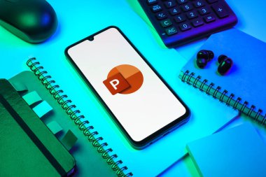 Prag, Çek Cumhuriyeti - 08 18 2025: Merkezde Powerpoint logosunu gösteren bir cep telefonu ile ofis malzemeleri düzenlemesi. Powerpoint sunumlar ve slayt gösterileri oluşturmak için bir yazılımdır..