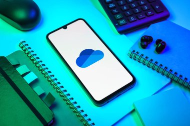 Prag, Çek Cumhuriyeti - 08 18 2025: Merkezde OneDrive logosunu gösteren bir cep telefonu ile ofis malzemeleri düzenlemesi. OneDrive dosyaları kaydetmek ve paylaşmak için bir bulut depolama platformudur.