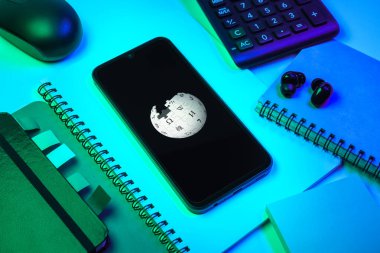 Prag, Çek Cumhuriyeti - 08 18 2025: Merkezinde Wikipedia logosu bulunan bir cep telefonu ile ofis malzemeleri düzenlemesi. Vikipedi çevrimiçi bir ansiklopedidir..
