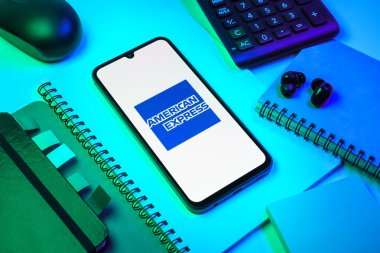 Prag, Çek Cumhuriyeti - 08 18 2025: Merkezde American Express logosunu gösteren bir cep telefonu ile ofis malzemeleri düzenlemesi. American Express kart ve bankacılık sunan bir finans şirketidir..