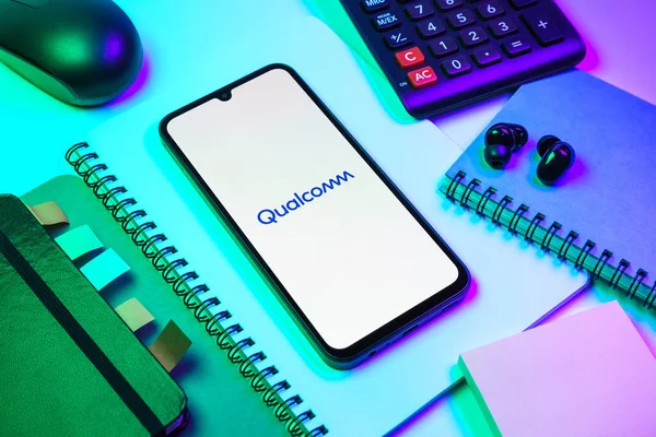 Prag, Çek Cumhuriyeti - 08 18 2025: Merkezde Qualcomm logosu sergilenen bir cep telefonu ile ofis malzemeleri düzenlemesi. Qualcomm, mobil çipler ve modemler üzerine uzmanlaşmış bir yarı iletken şirketidir..