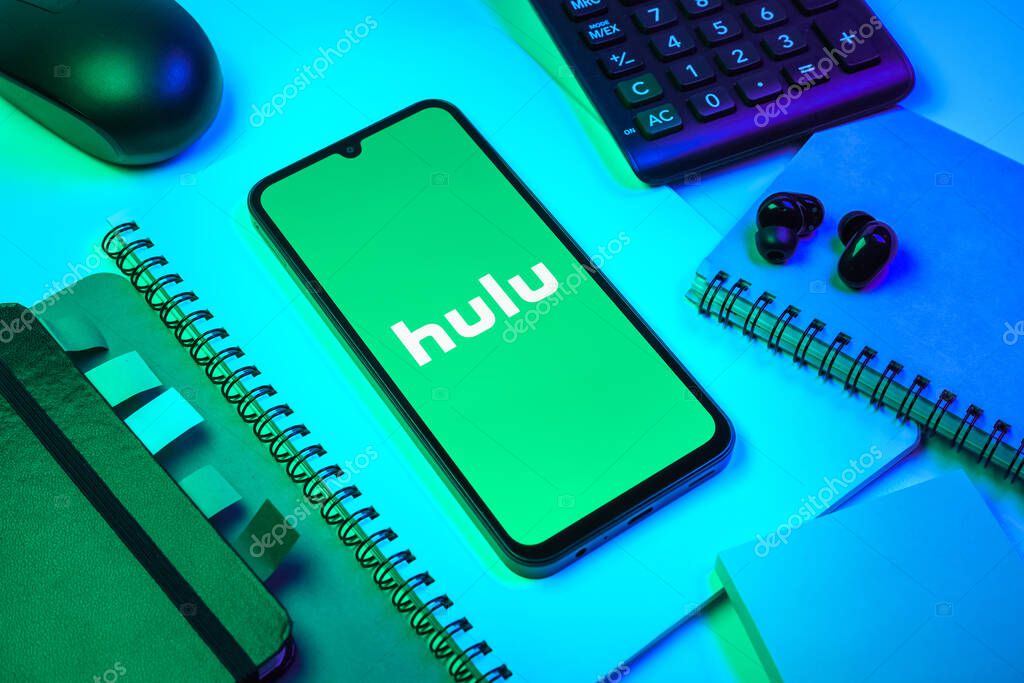 Prague, Czechia - 08 18 2025: An arrangement of office supplies with a mobile phone in the center displaying Hulu logo. Hulu is a streaming platform for TV shows, movies, and live TV.