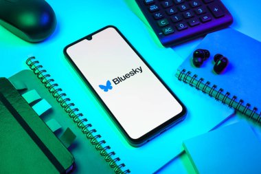 Prag, Çek Cumhuriyeti - 08 18 2025: Merkezde Bluesky logosunu gösteren bir cep telefonu ile ofis malzemeleri düzenlemesi. Bluesky merkezi olmayan ağlar için bir sosyal medya platformudur..
