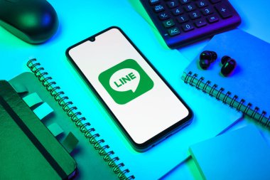 Prag, Çek Cumhuriyeti - 08 18 2025: Merkezinde hat logosu sergilenen bir cep telefonu ile ofis malzemeleri düzenlemesi. Line aramalar, mesajlar ve çokluortam paylaşımı için bir mesajlaşma uygulamasıdır.