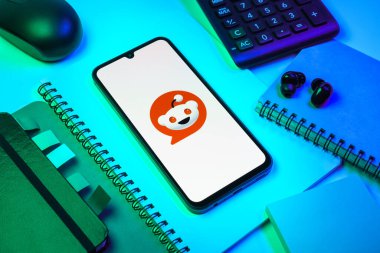 Prag, Çek Cumhuriyeti - 08 18 2025: Merkezde Reddit logosunu gösteren bir cep telefonu ile ofis malzemeleri düzenlemesi. Reddit tartışma, haber ve toplum içeriği için bir platformdur.