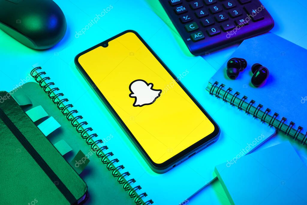 Prague, Czechia - 08 18 2025: An arrangement of office supplies with a mobile phone in the center displaying Snapchat logo. Snapchat is an app for sending photos, videos, and temporary messages.