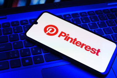 Prag, Çek Cumhuriyeti - 09 02 2025: Pinterest logosunun renkli ışıklarla aydınlatıldığı dizüstü bilgisayardaki telefon. Pinterest fikirleri görsel olarak keşfetmek ve kaydetmek için bir platformdur..