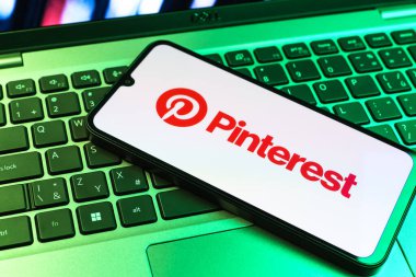 Prag, Çek Cumhuriyeti - 09 02 2025: Pinterest logosunun renkli ışıklarla aydınlatıldığı dizüstü bilgisayardaki telefon. Pinterest fikirleri görsel olarak keşfetmek ve kaydetmek için bir platformdur..