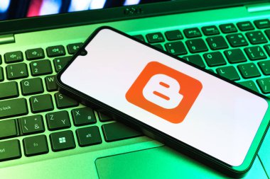 Prag, Çek Cumhuriyeti - 09 02 2025: Renkli ışık tarafından aydınlatılan dizüstü bilgisayardaki telefon blogger logosunu gösteriyor. Blogger blog oluşturma ve yayınlama için bir platformdur.