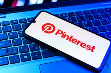Prag, Çek Cumhuriyeti - 09 02 2025: Pinterest logosunun renkli ışıklarla aydınlatıldığı dizüstü bilgisayardaki telefon. Pinterest fikirleri görsel olarak keşfetmek ve kaydetmek için bir platformdur..