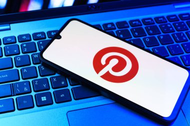 Prag, Çek Cumhuriyeti - 09 02 2025: Pinterest logosunun renkli ışıklarla aydınlatıldığı dizüstü bilgisayardaki telefon. Pinterest fikirleri görsel olarak keşfetmek ve kaydetmek için bir platformdur..