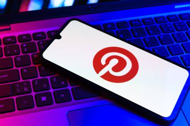 Prag, Çek Cumhuriyeti - 09 02 2025: Pinterest logosunun renkli ışıklarla aydınlatıldığı dizüstü bilgisayardaki telefon. Pinterest fikirleri görsel olarak keşfetmek ve kaydetmek için bir platformdur..