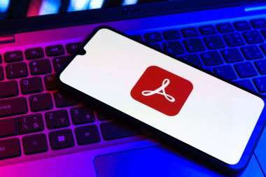 Prag, Çek Cumhuriyeti - 09 02 2025: Renkli ışık tarafından aydınlatılan dizüstü bilgisayardaki telefon Akrobat Reader logosunu gösteriyor. Acrobat Reader, PDF belgelerini görüntülemek ve yönetmek için bir platformdur.